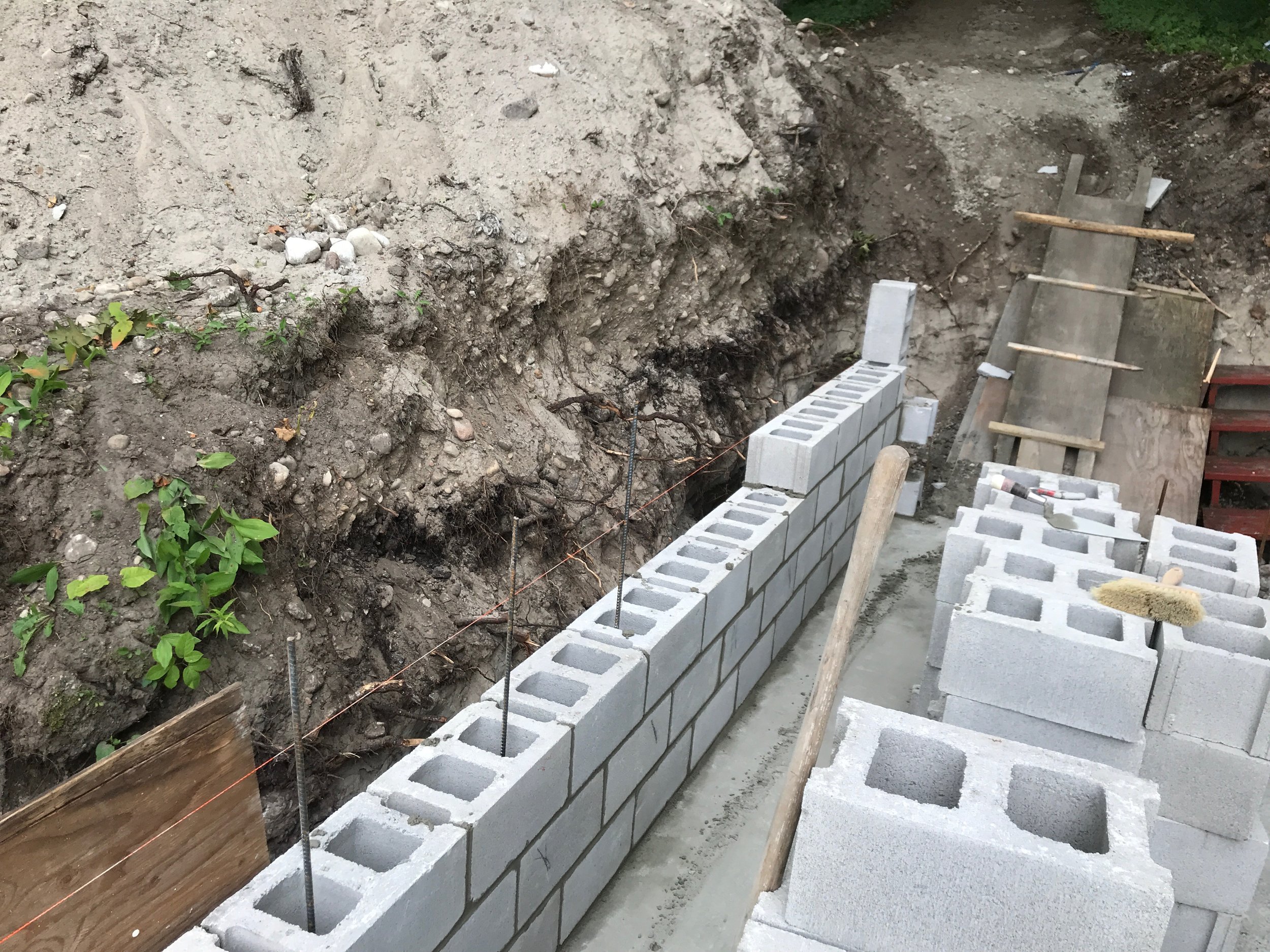 Foundation construction site with concrete blocks being laid for a wall, and an excavated dirt trench adjacent to the blocks.