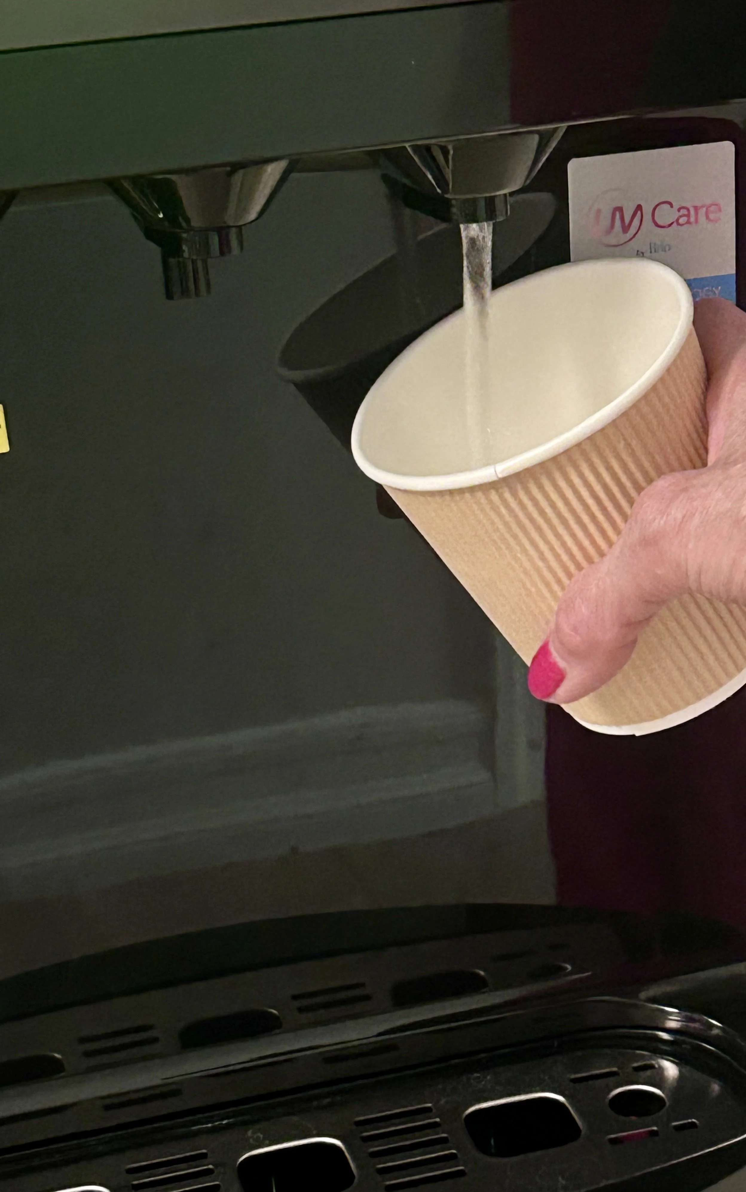 A person is holding a paper cup under a water dispenser, filling it with liquid in a therapy office for rent in Brooklyn.