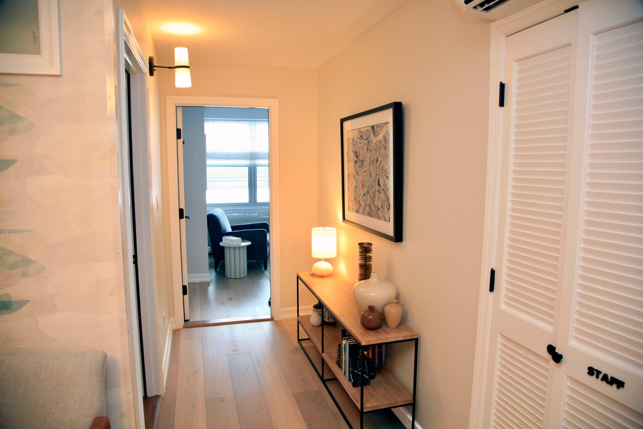 View of waiting room hallway in therapy office for rent in Brooklyn. There is a wooden console table with vases and a lamp and framed art on the wall.