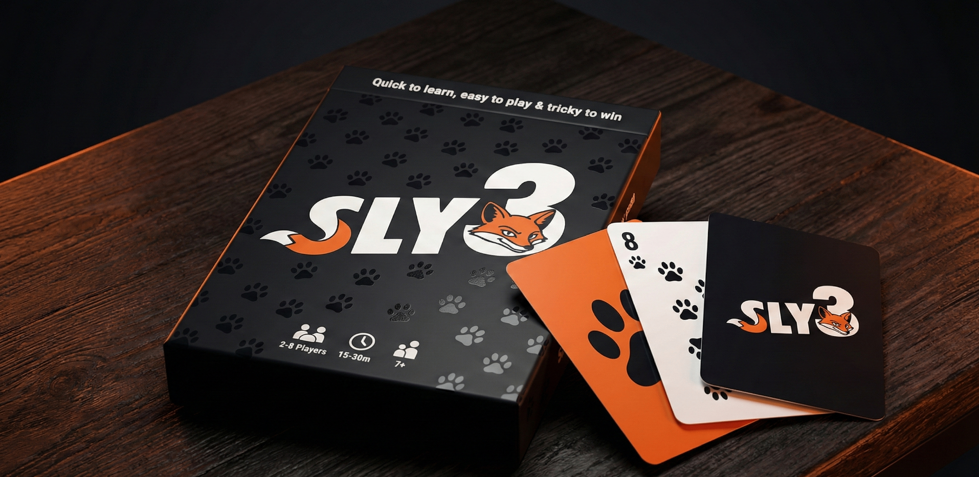The Sly 3 card game box on a wooden surface, with three cards displayed: 8 of paw prints, 4 of paw prints, and the game box featuring a fox face logo and paw prints.