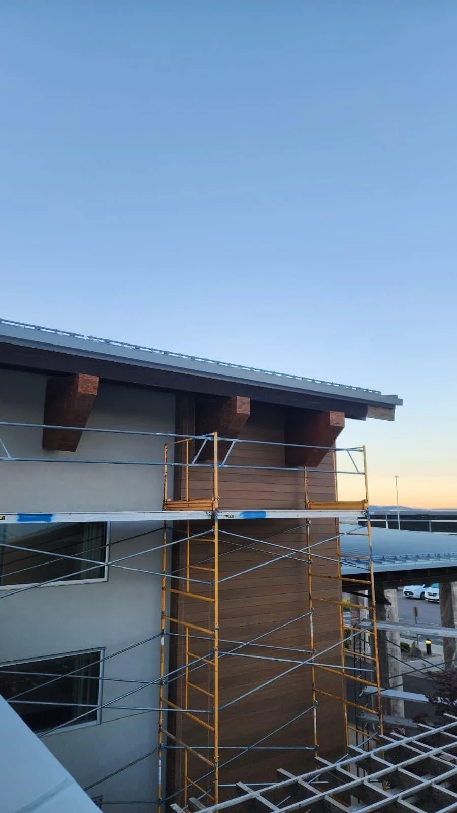 Building under construction with scaffolding, showing a modern multi-story structure with a flat roof, wooden accents, and large window openings, set against a clear evening sky.
