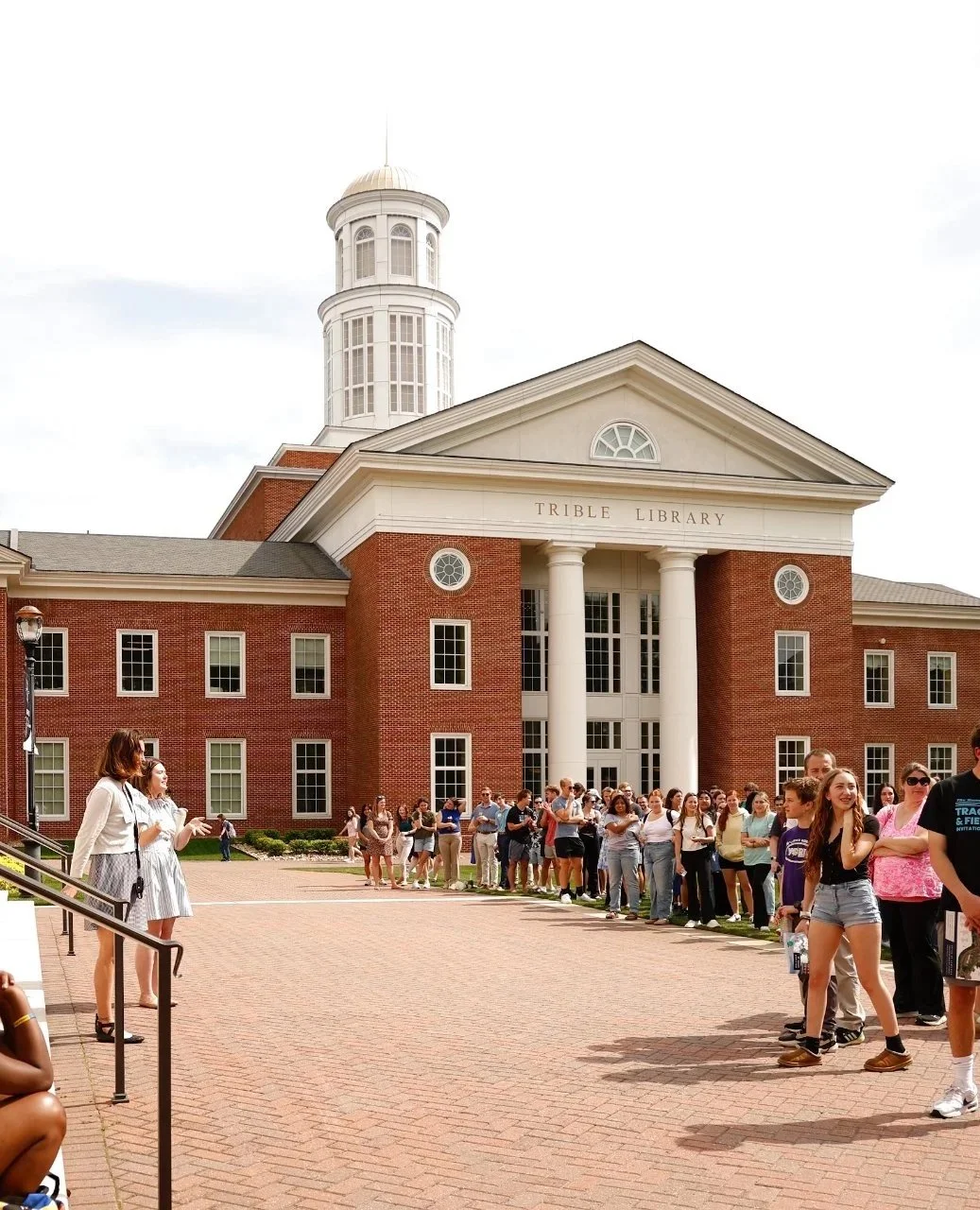 Line of people waiting outside Trible Library, a red brick building with white columns and a large cupola.