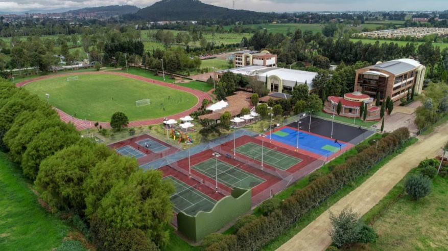 Overview of a school campus with athletic fields, tennis courts, and surrounding greenery.