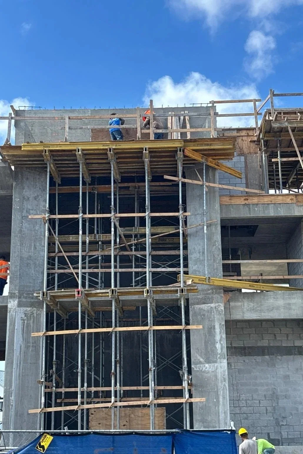 Construction workers on a multi-story building under construction with scaffolding and a blue sky in the background.