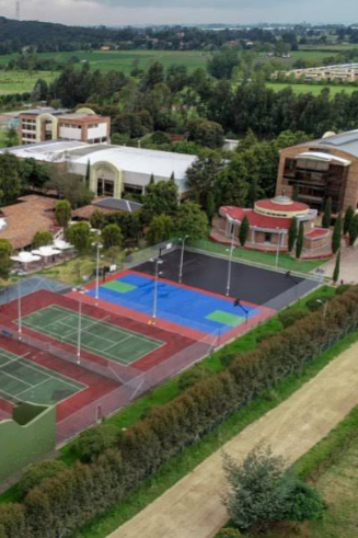A sports complex with multiple tennis courts and a colorful basketball court, surrounded by trees and greenery, with several modern buildings in the background.