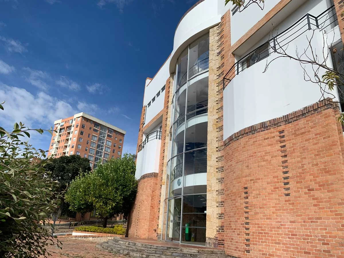 Low-angle view of modern residential building with curved brick wall, glass elevator shaft, and balcony railings, under a blue sky with some clouds.