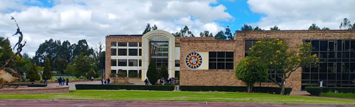 A school building with a brick facade, large glass windows, and a central entrance, surrounded by trees and a grassy area, under a partly cloudy sky.