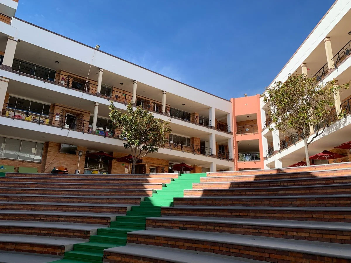 View of a multi-story apartment complex with brick walls, balconies, and trees in the courtyard, under a clear blue sky.