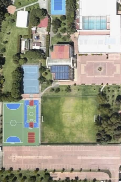 Aerial view of a sports complex with multiple basketball courts, tennis courts, a large open field, a swimming pool area, and surrounding buildings and greenery.