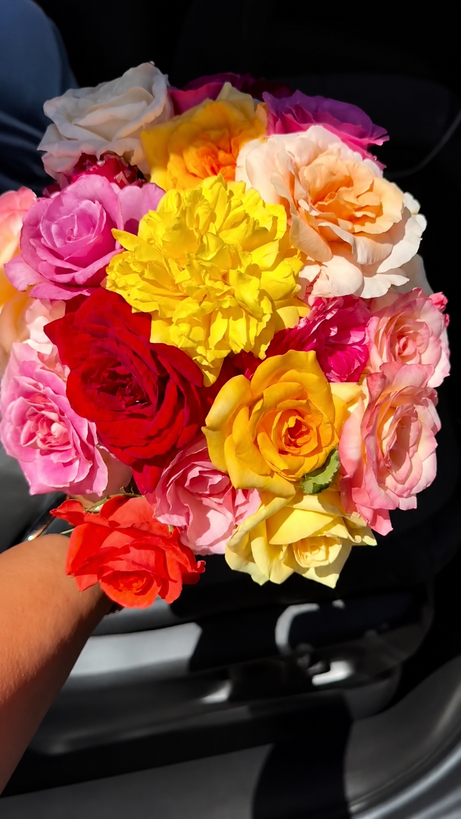 A colorful bouquet of various roses and a yellow flower, being held by a person's hand.