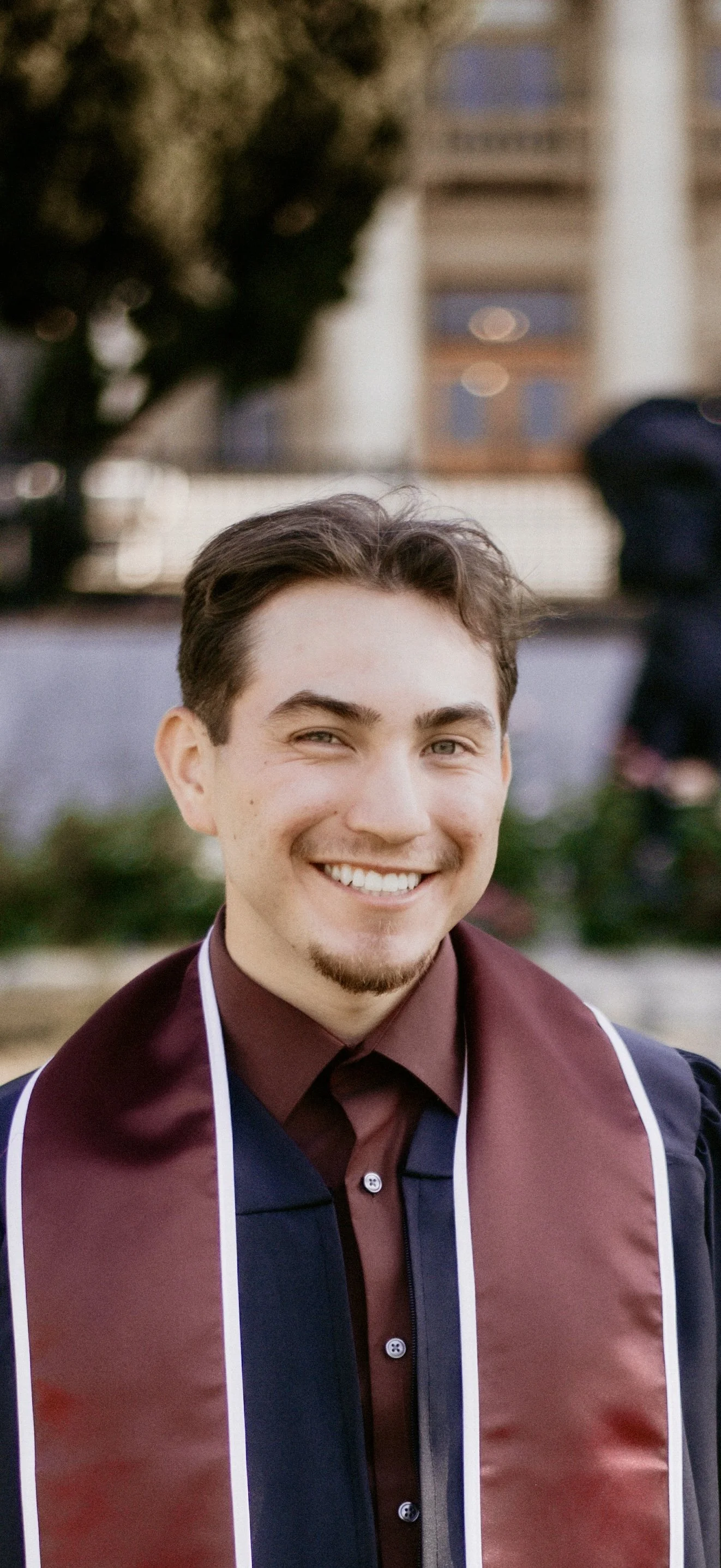 Young man in graduation gown smiling outdoors.