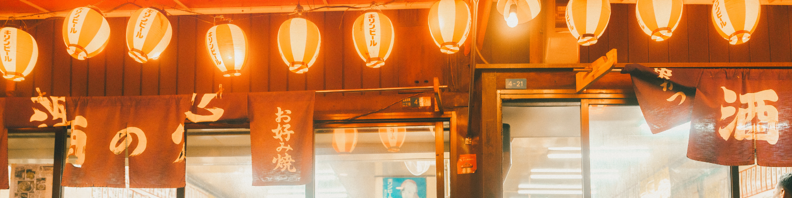 Japanese-style restaurant entrance decorated with orange paper lanterns and red noren curtains with white Japanese characters.