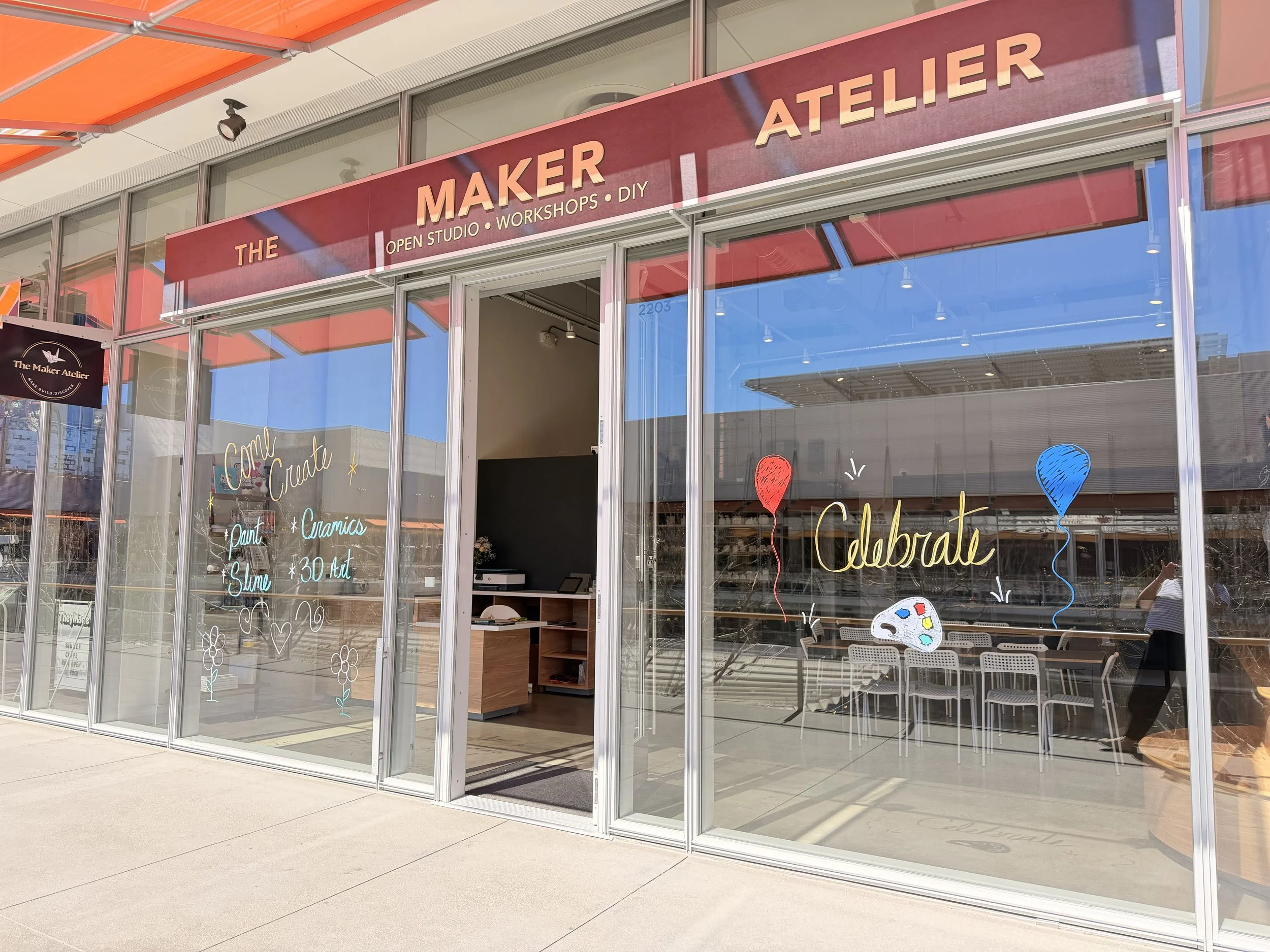 The storefront of The Maker Atelier, a DIY workshop and open studio, decorated with colorful hand-drawn balloons, art palette, and cheerful illustrations, celebrating creativity and artistic activities.