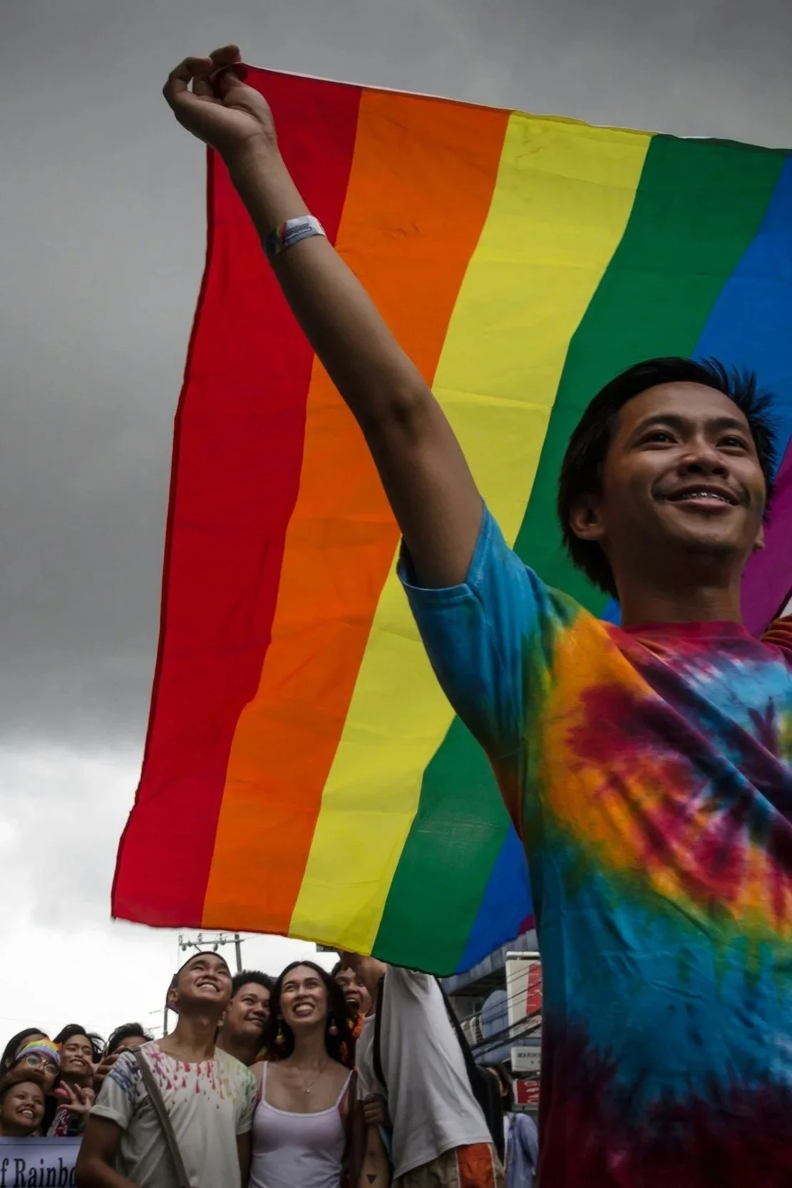 A person holds a rainbow pride flag at a pride parade, with a group of smiling people in the background.