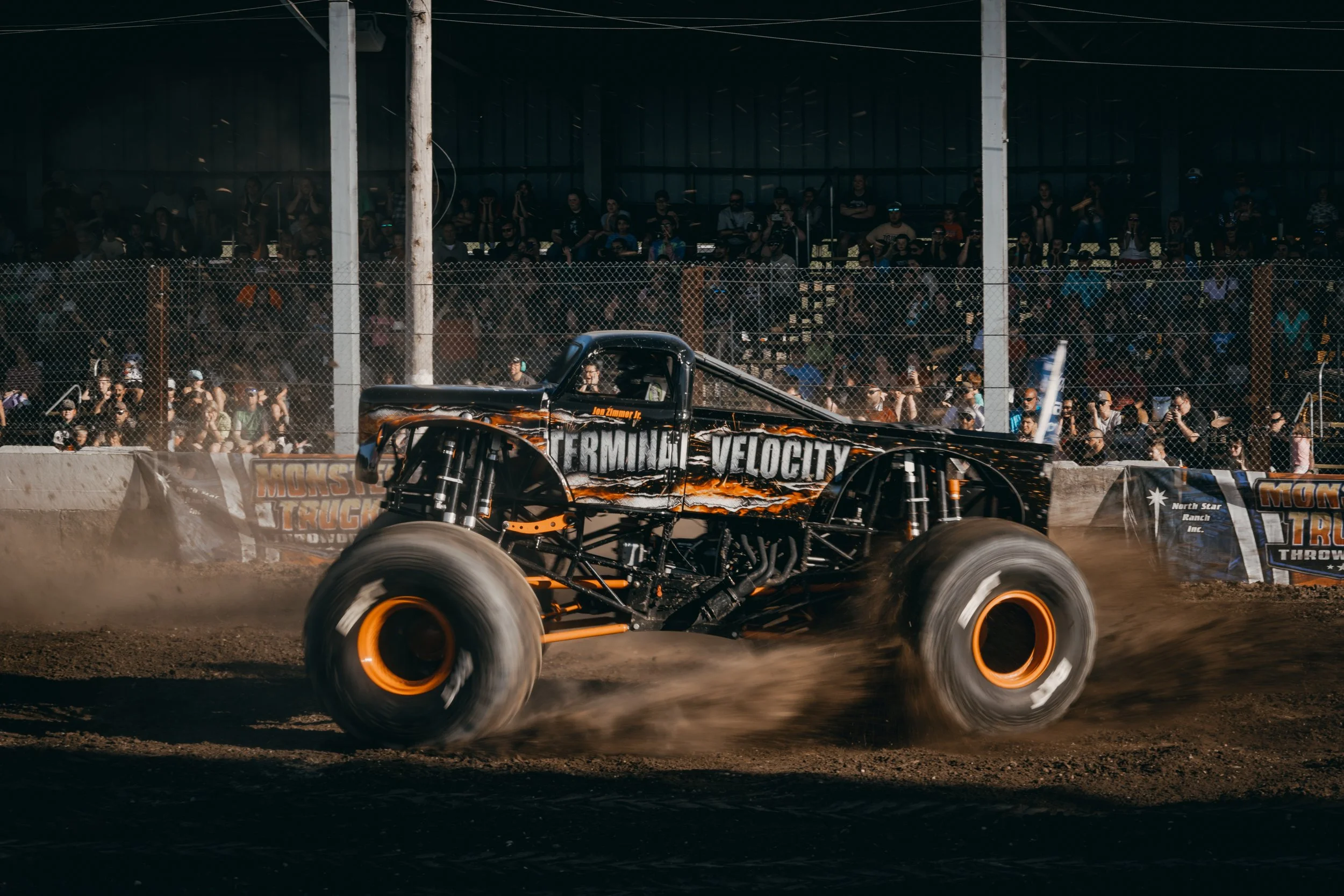 A monster truck called 'Terminator Velocity' racing on a dirt track with a crowd watching from the stands.