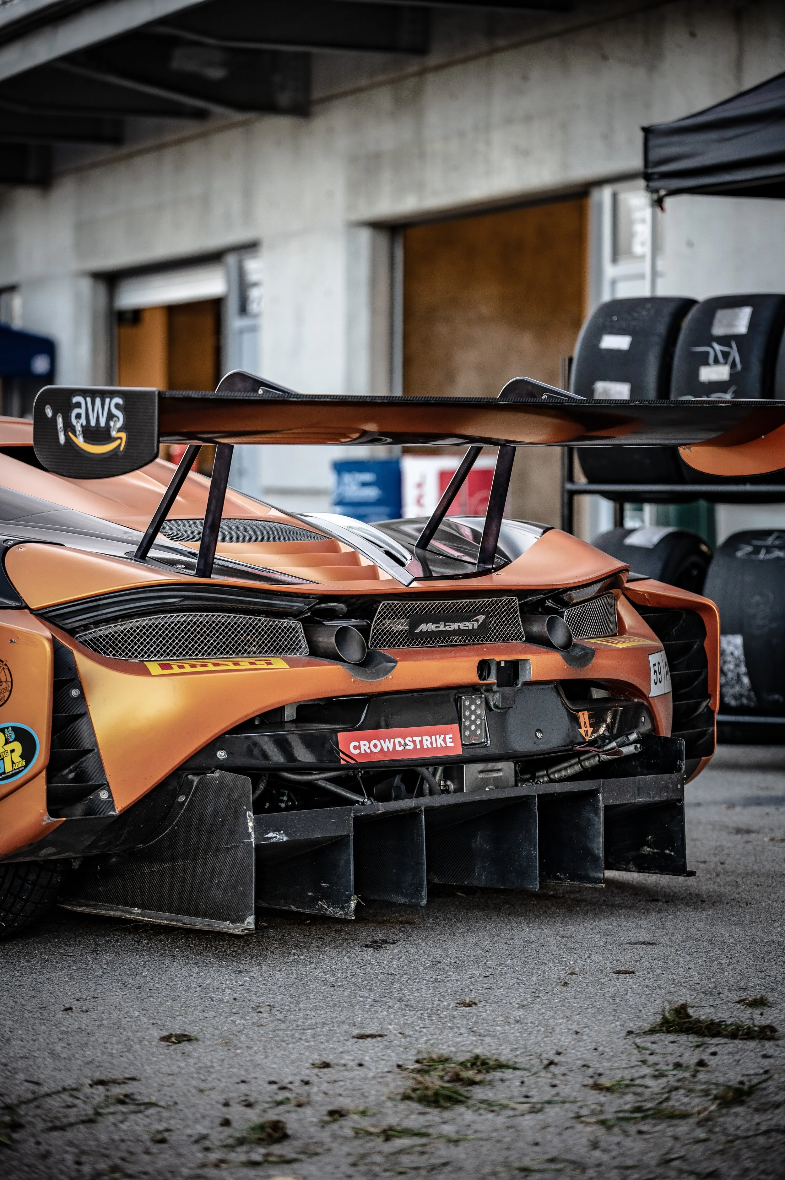 Orange race car with a large rear wing and aero elements parked in a garage area.