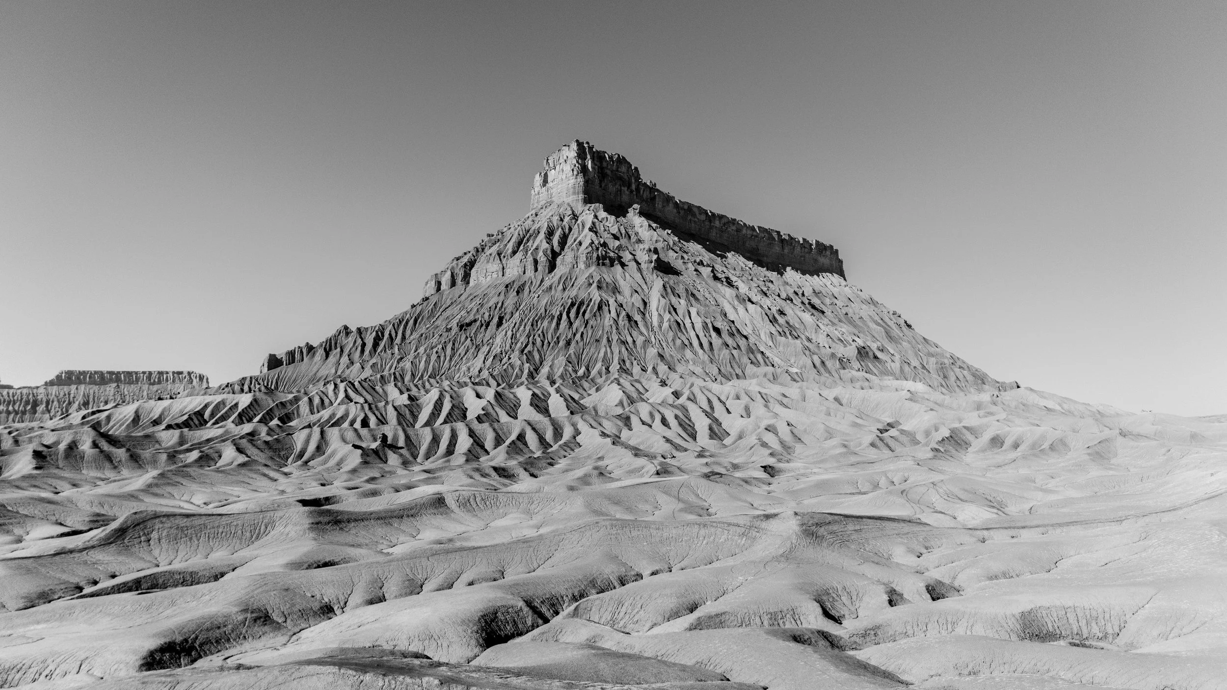 Black-and-white photo of a flat-topped mountain with ridges and slopes leading up to a fortress-like structure at the peak, desert terrain in foreground.