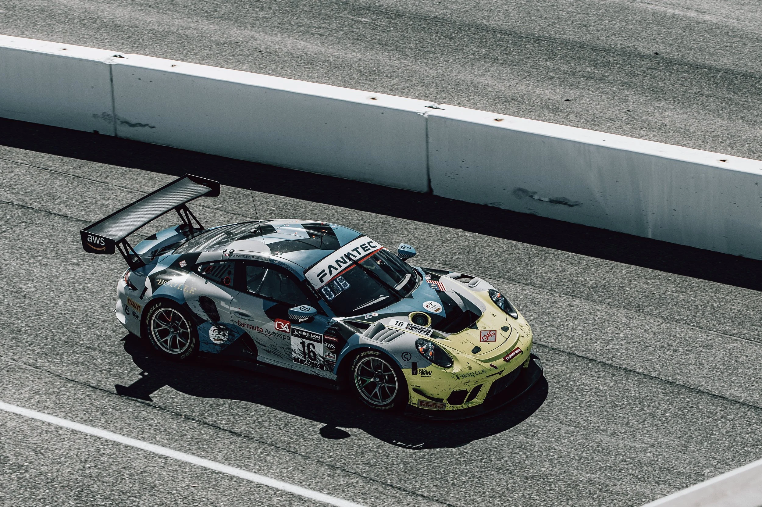 A race car on a racetrack, positioned next to a white safety barrier, with various sponsor logos and the number 16 displayed on the sides and front.