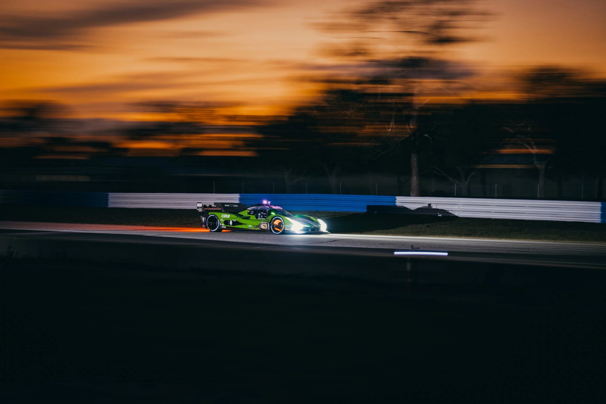 A race car speeding on a track at sunset with blurred trees in the background.