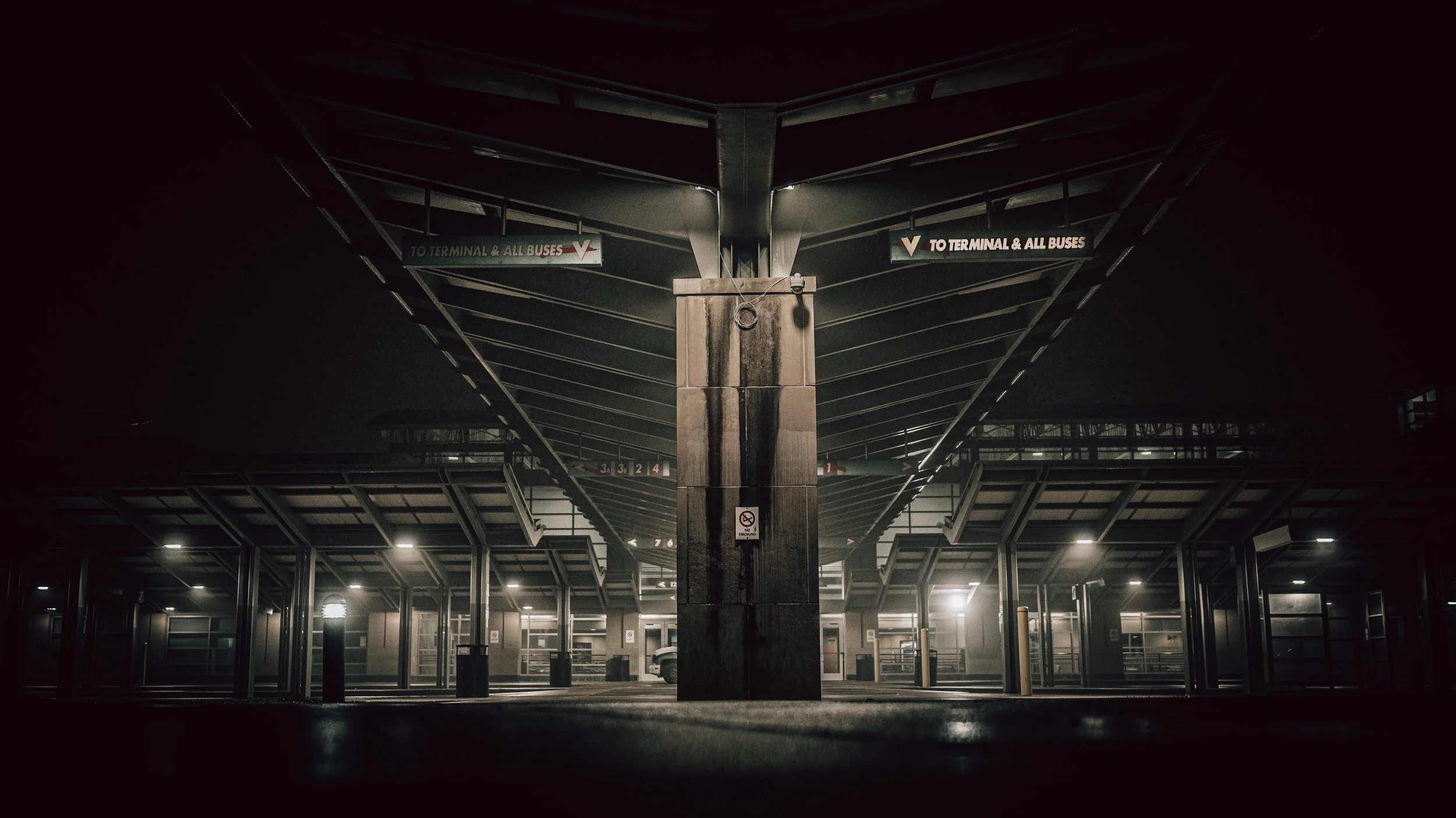 Empty parking garage at night with overhead lights, structural pillars, and signs directing to terminals and buses.