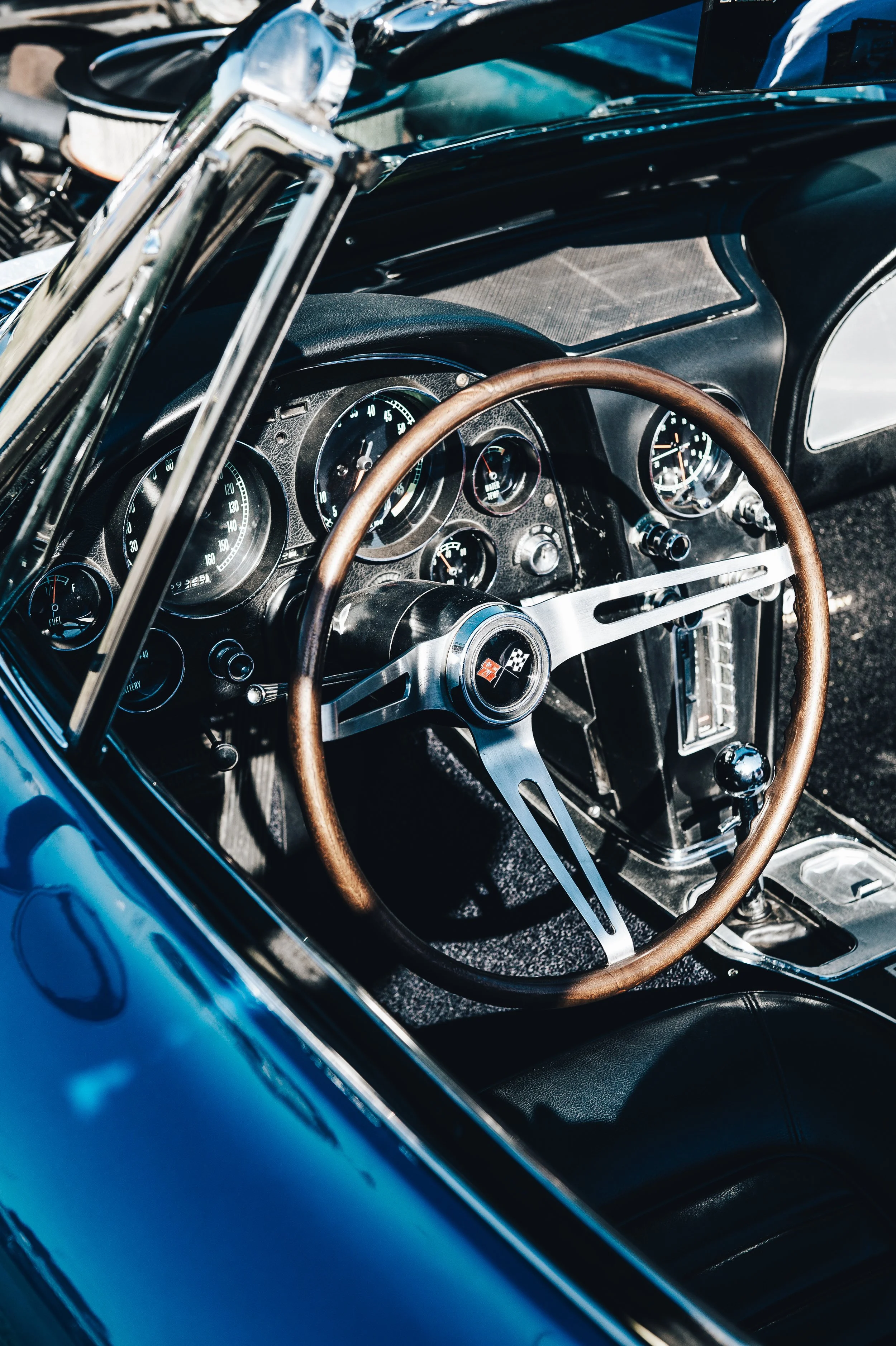 Close-up of the interior dashboard and steering wheel of a vintage Chevrolet Corvette with wood accents and classic instrumentation.