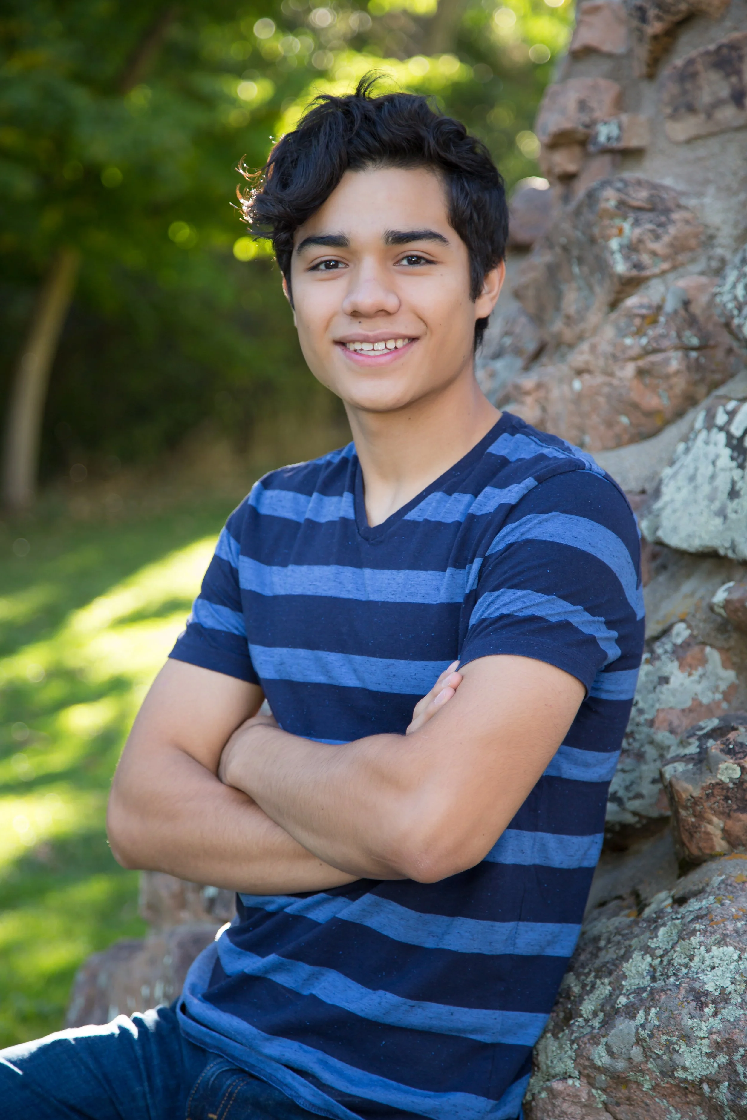 An outdoor high school senior portrait session featuring a smiling young man sitting on a stone wall on location at Chautauqua Park in Boulder, Colorado, by Lisa Doane Photography.