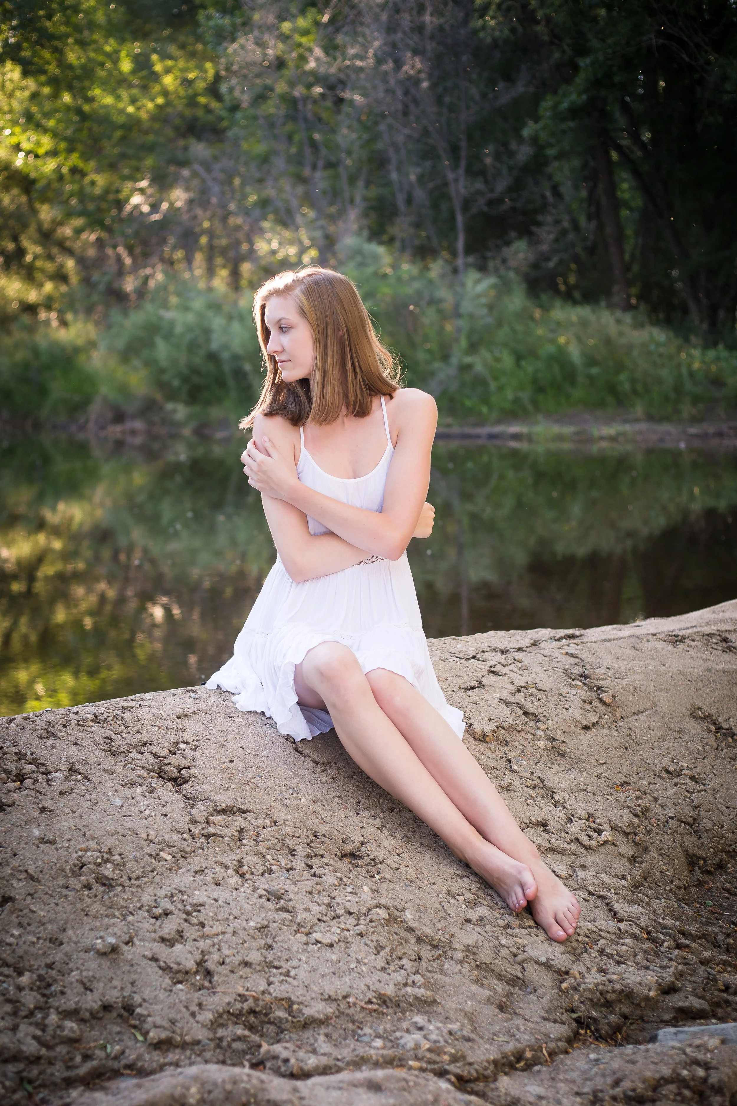 An intentional high school senior portrait session of a girl sitting on the waterfall dam giving herself a self-love hug at Golden Ponds Nature Area in Longmont, Colorado.