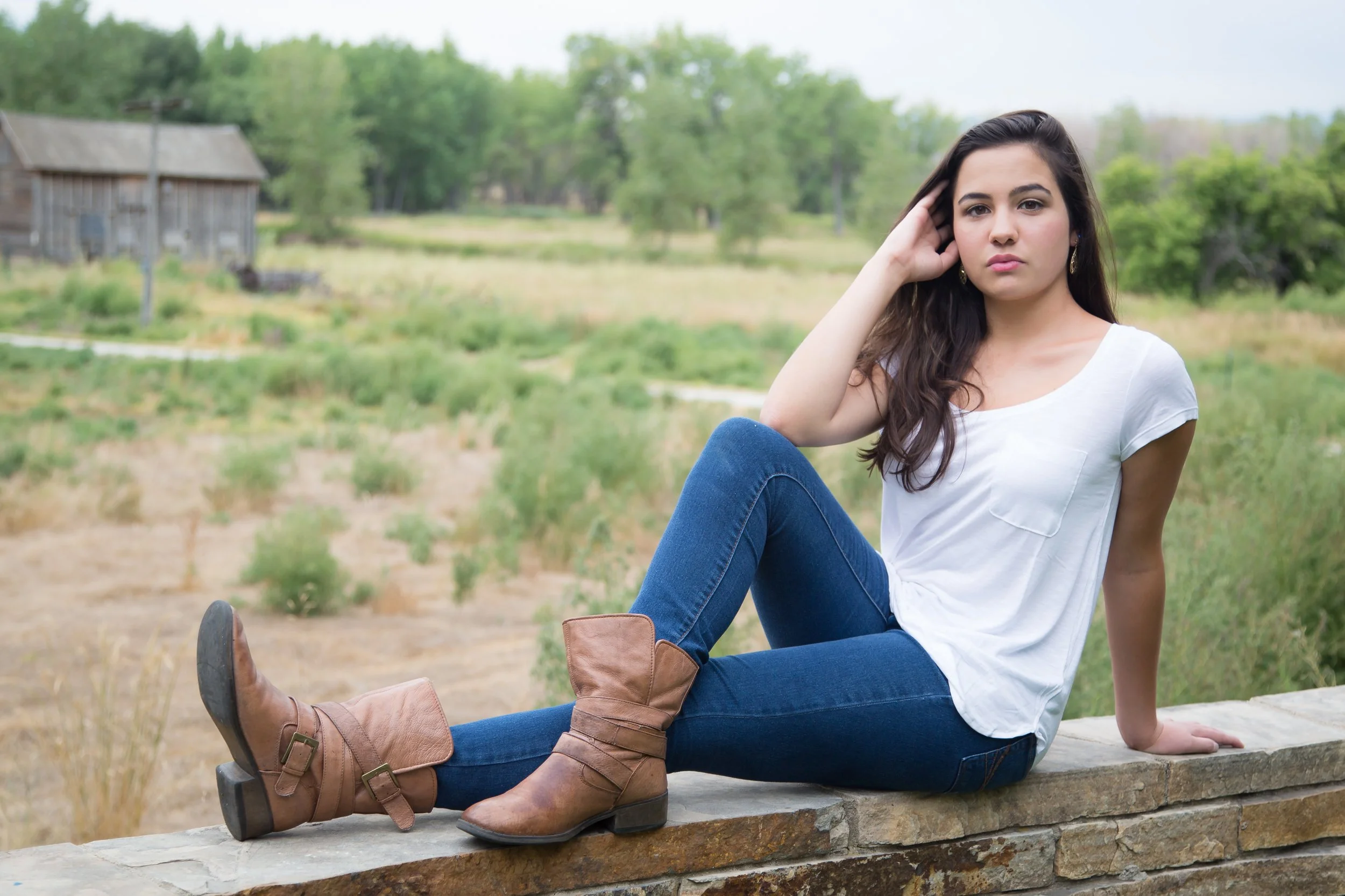 A rustic high school senior portrait session of a young woman sitting on a stone ledge at the historic Morse Coffin homestead at Sandstone Ranch Visitors Center in Longmont, Colorado.