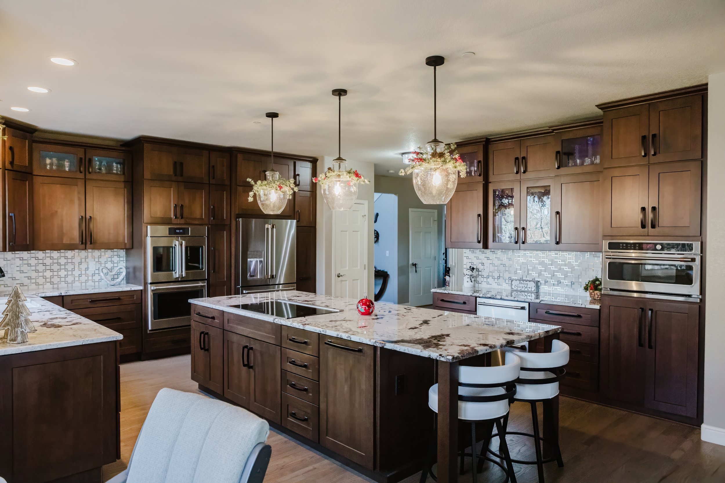Modern kitchen with wooden cabinetry, granite island, pendant lighting, and holiday decorations.