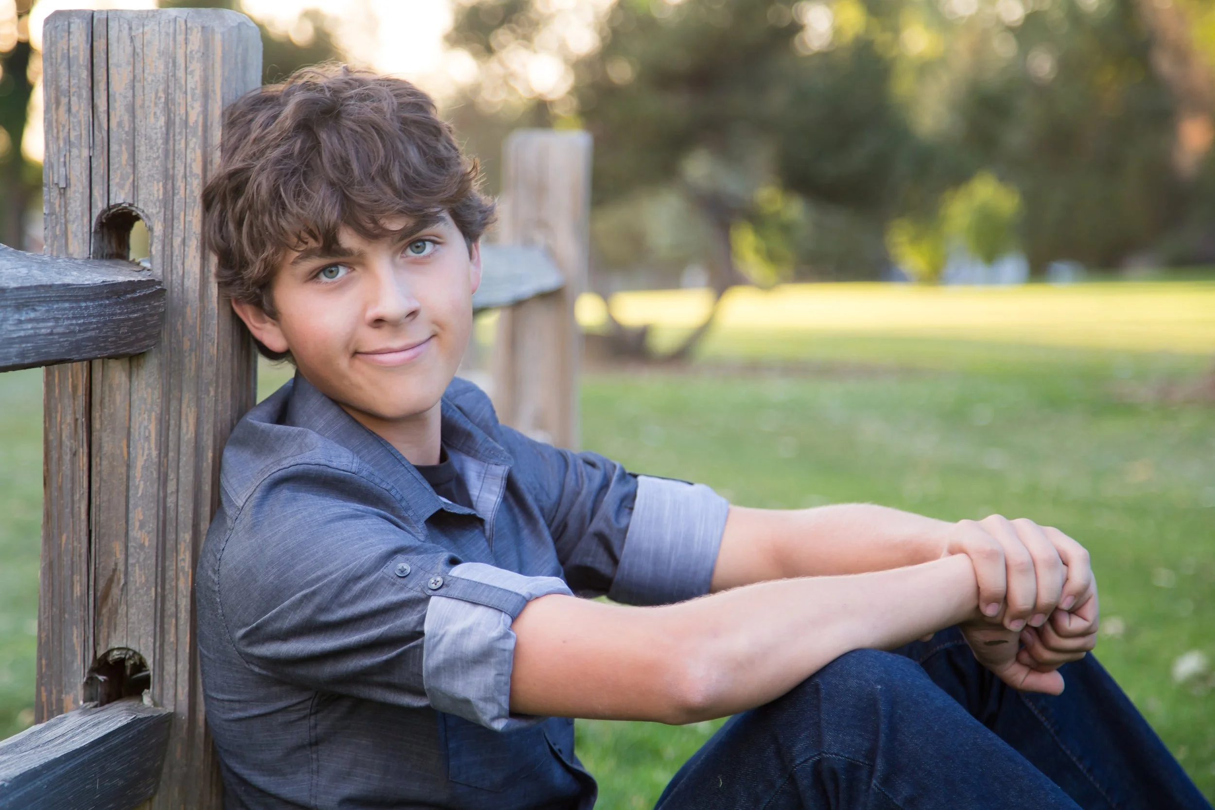 An outdoor high school senior portrait session of a boy leaning against a rustic wooden fence during sunset at Sunset Golf Course in Longmont, Colorado, captured by Lisa Doane Photography.