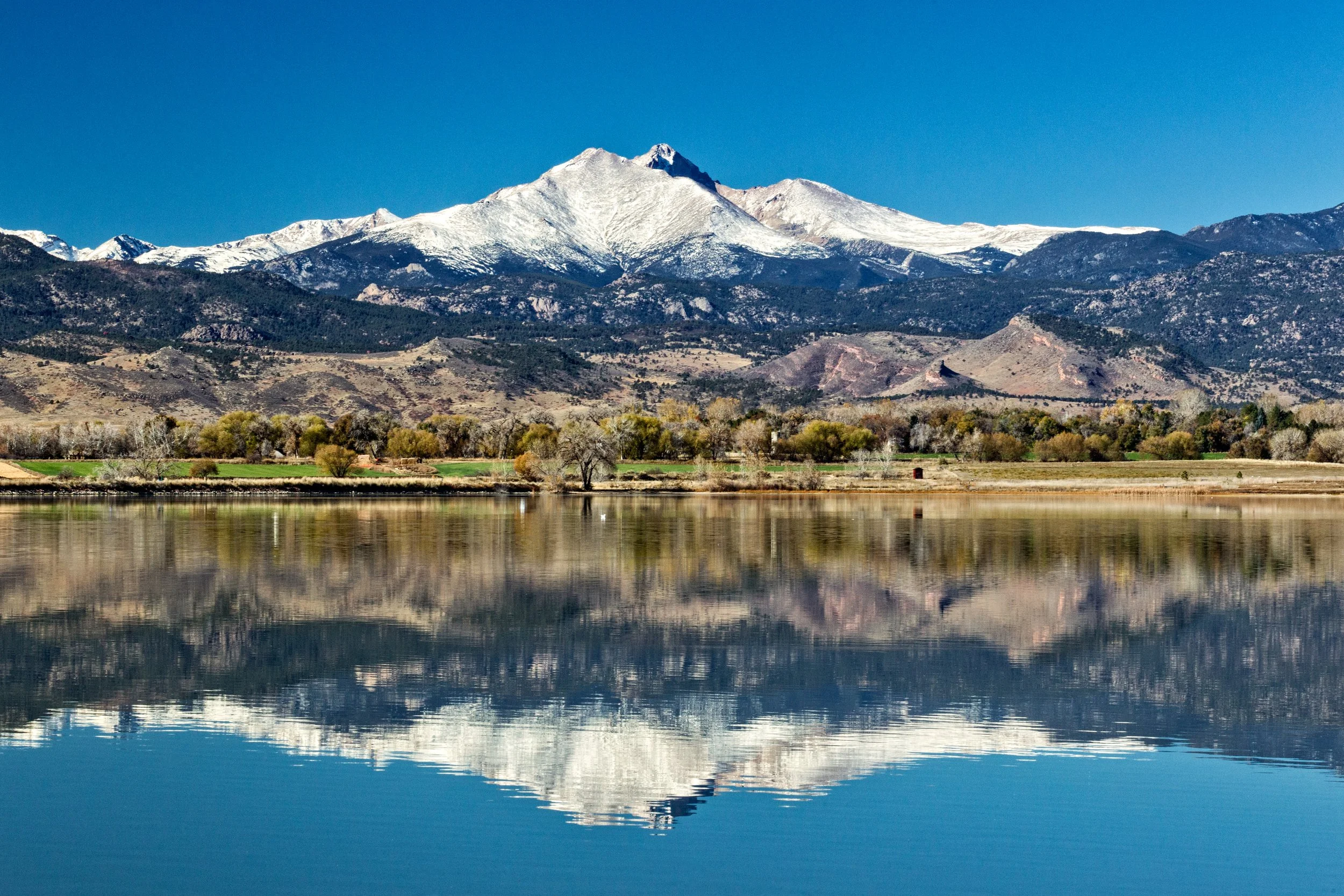 Fine art landscape photography of Longs Peak and Mount Meeker with a perfect mirror reflection on the calm water of McIntosh Lake in Longmont, Colorado.