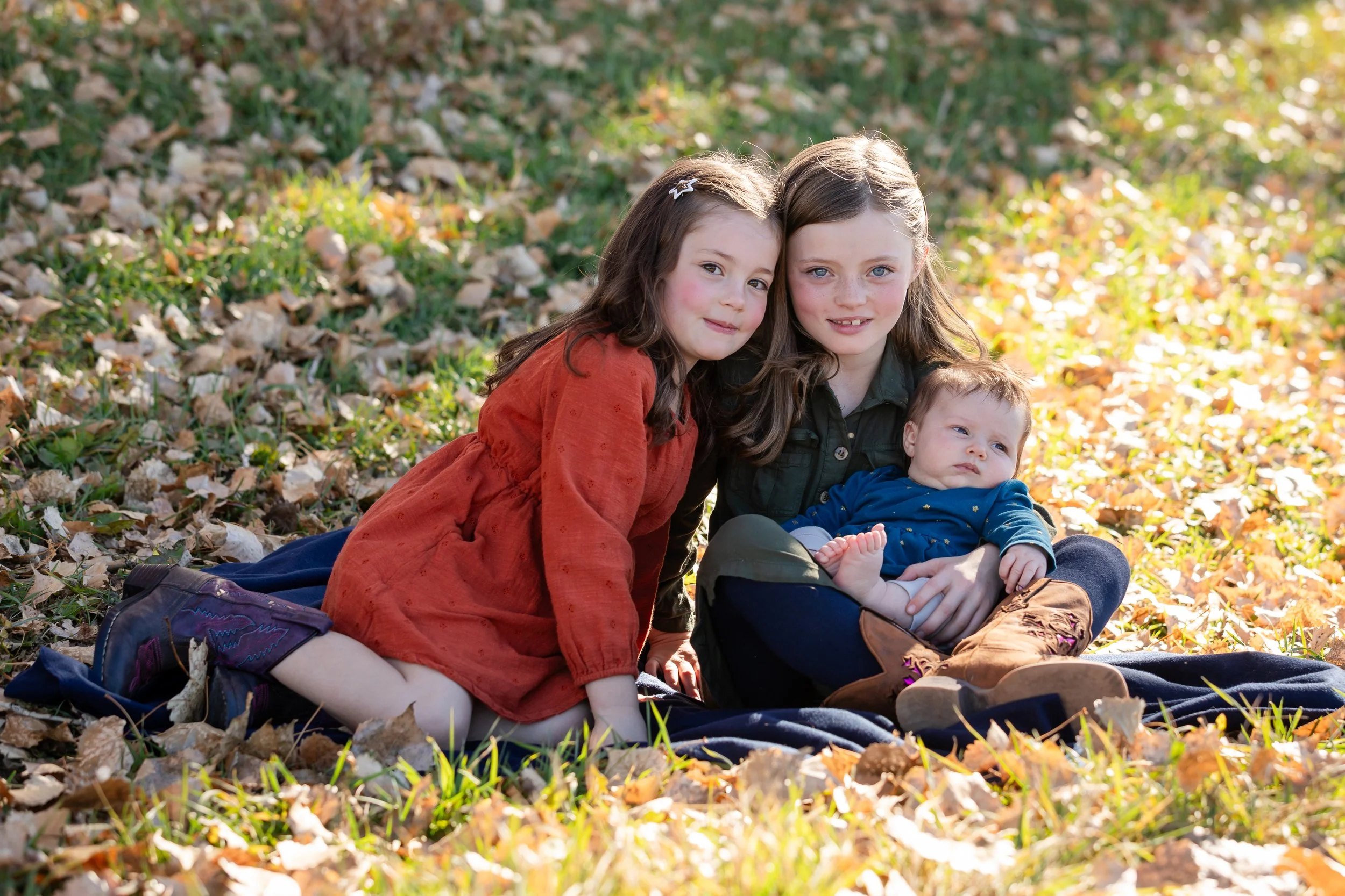 A classic outdoor autumn sibling portrait session featuring three children sitting together on a blanket on their family farm in Longmont, Colorado, by Lisa Doane Photography.