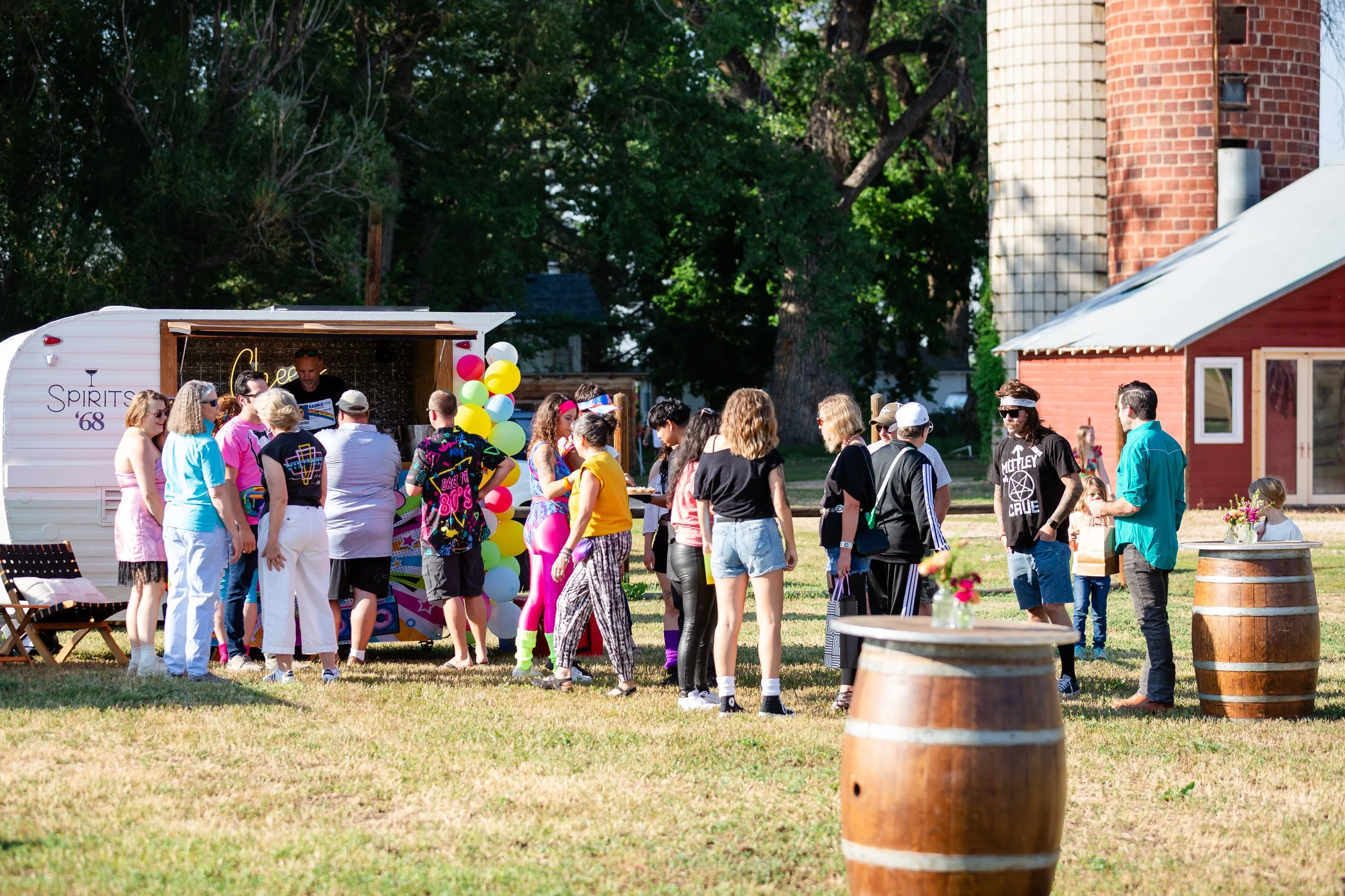 Documentary event photography of guests gathered outdoors near a decorated vintage mobile bar trailer at an 80s themed birthday party hosted at Old Elm Farm in Boulder, Colorado, by Lisa Doane Photography.