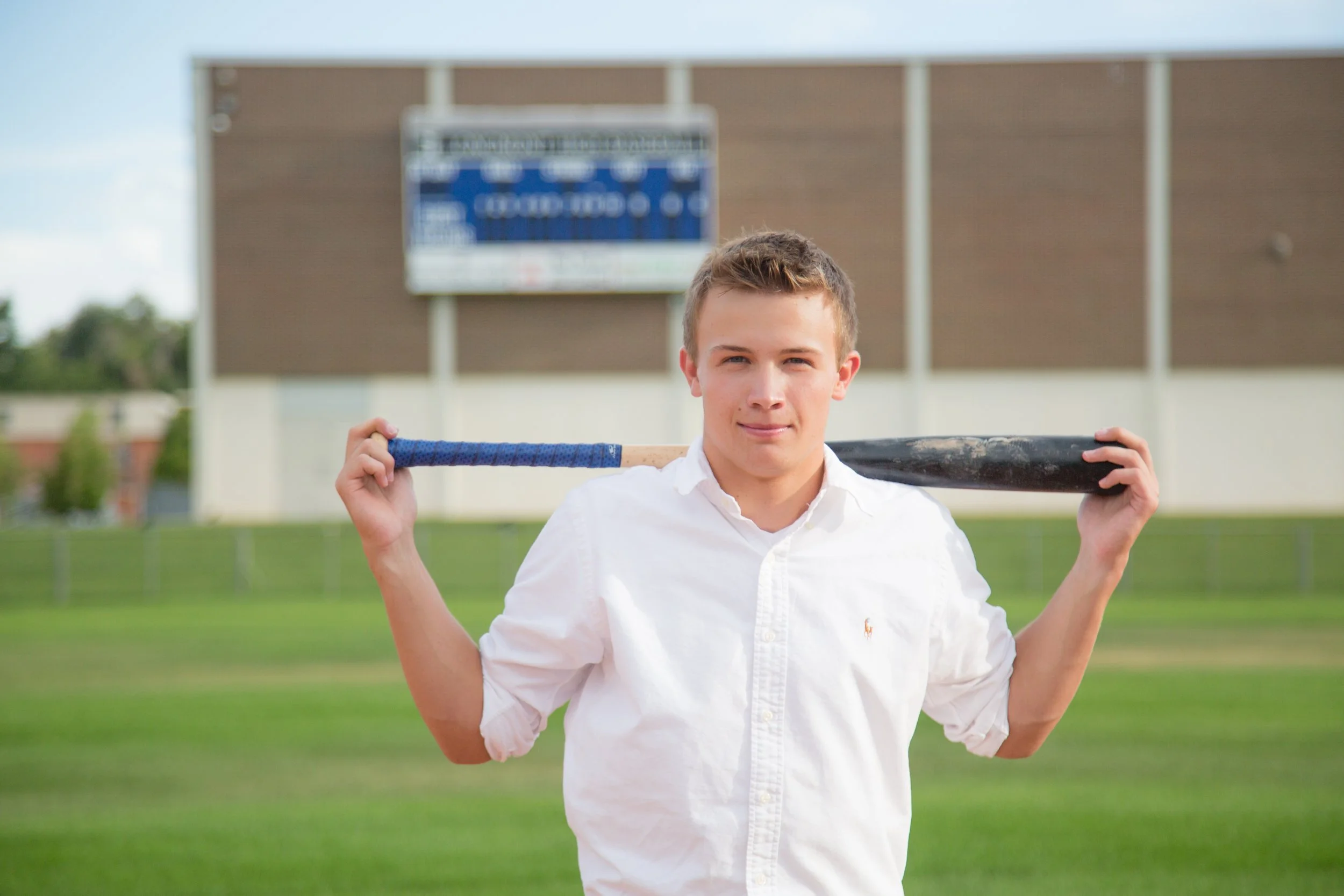 A dynamic male high school senior portrait session featuring a baseball player holding a bat on the baseball diamond at Longmont High School in Longmont, Colorado, by Lisa Doane Photography.