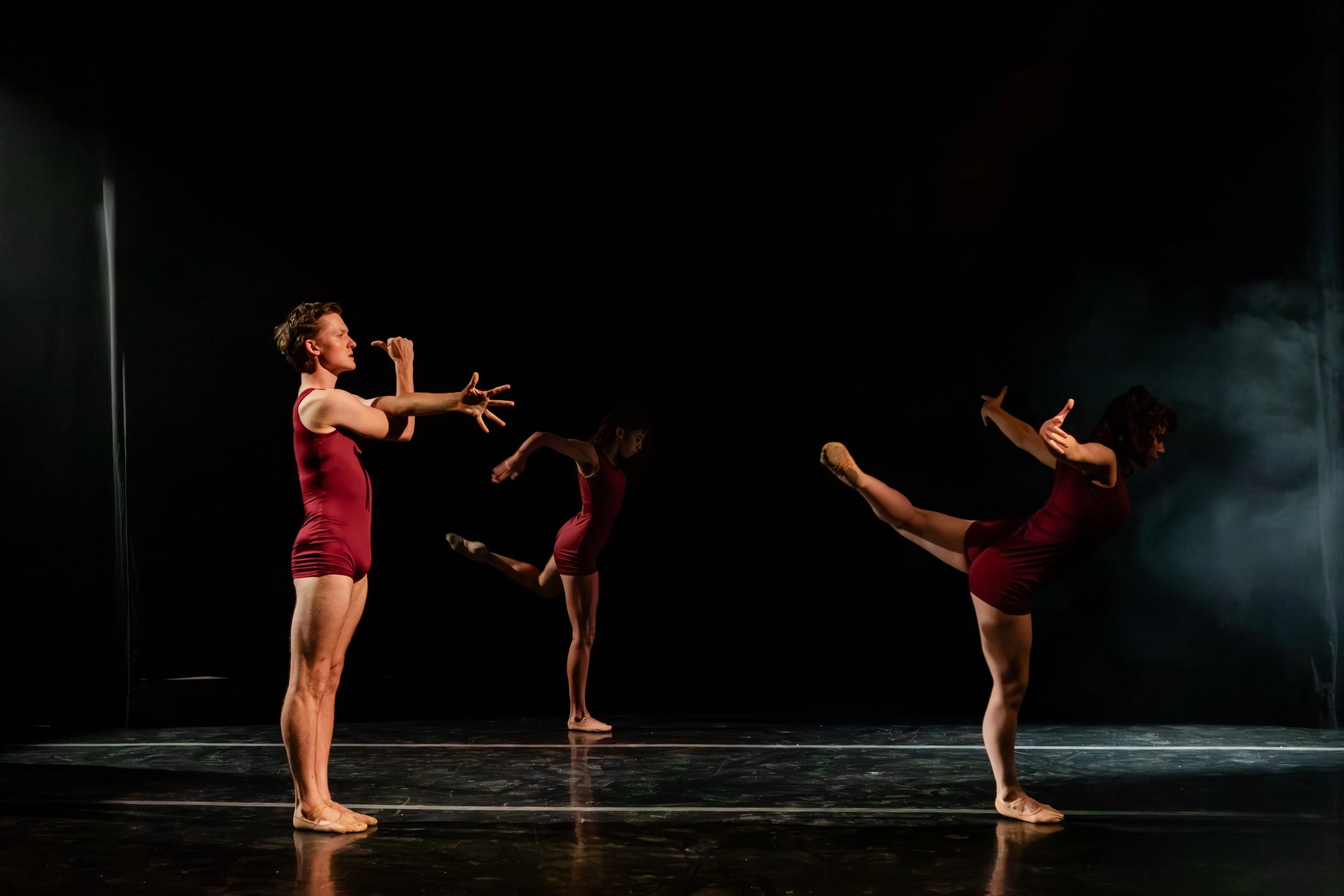 Professional performance photography by Lisa Doane Photography of the dynamic modern dance festival Dance Continua at The Spark in Boulder, Colorado. Three dancers are depicted in maroon singlets on a dark, dramatically lit stage.