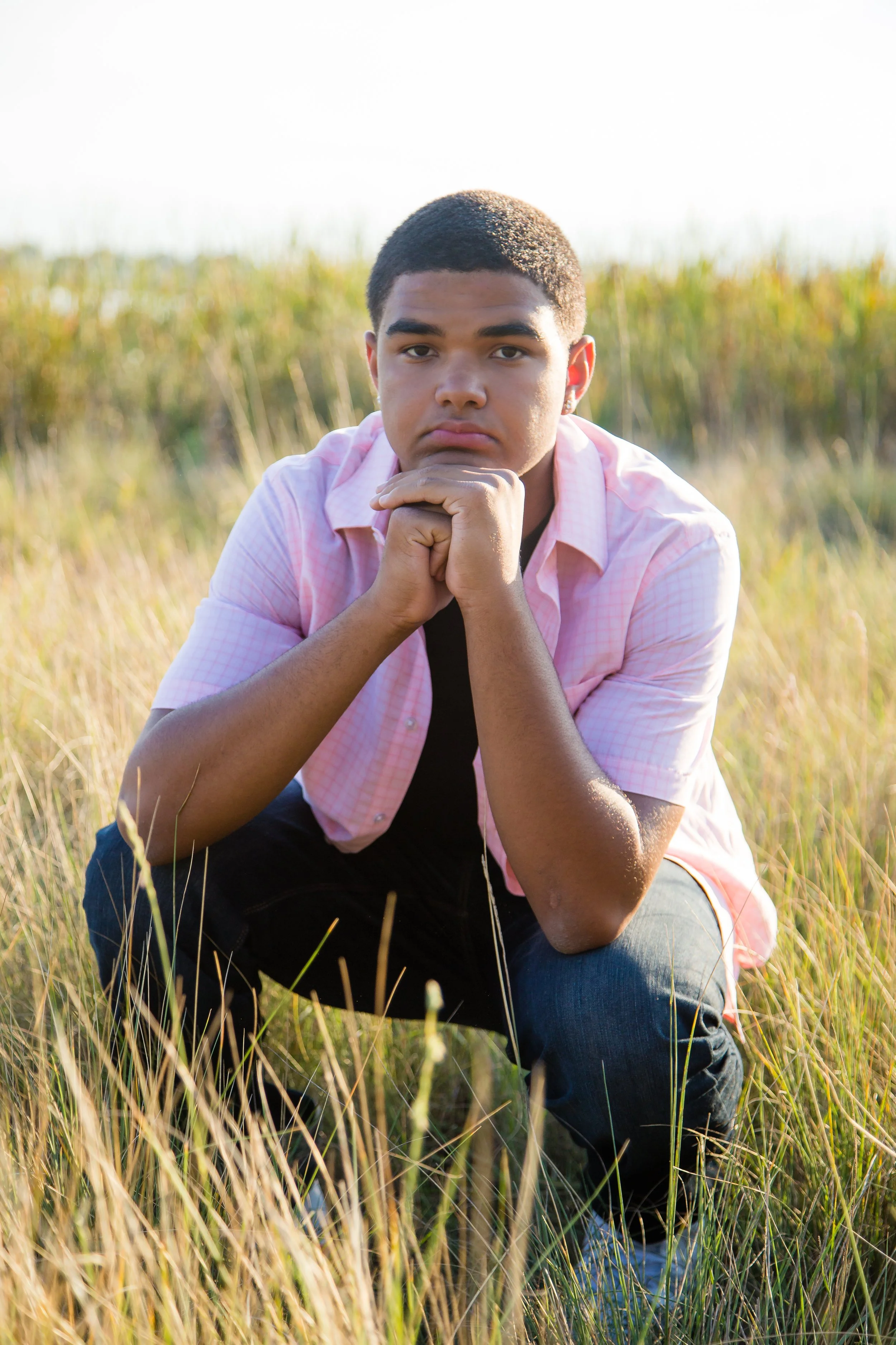 A high school senior portrait session captured during a warm golden hour, featuring a young man kneeling in a grassy field on location at McIntosh Lake in Longmont, Colorado.