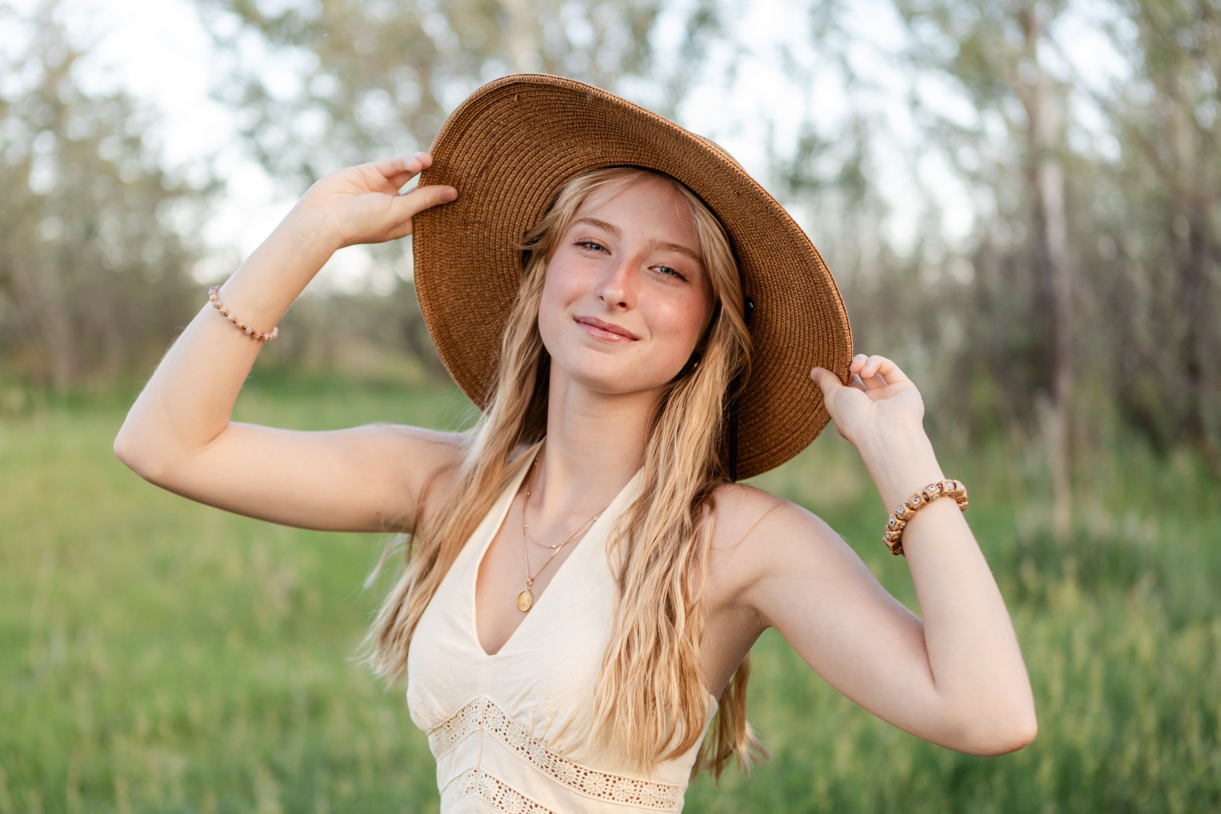 High school senior portrait taken in soft natural light at Coot Lake, featuring a young lady wearing a woven sun hat and a cream sundress during her outdoor session.