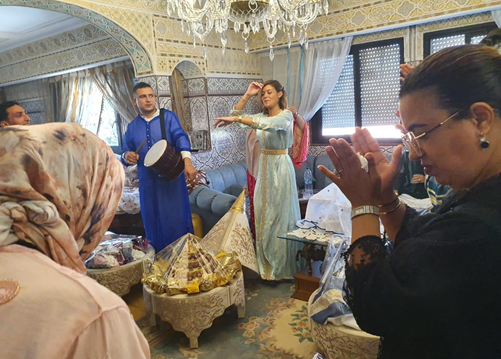 People participating in a traditional celebration or prayer ritual in a decorated room with ornate walls and a chandelier.