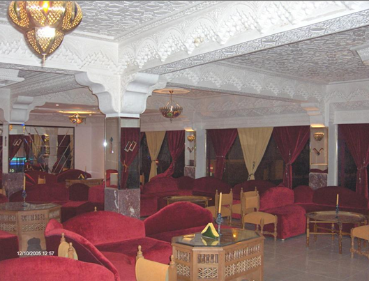 Interior of a lounge or cafe with cushioned seating, ornate ceiling decorations, and curtains along the windows.