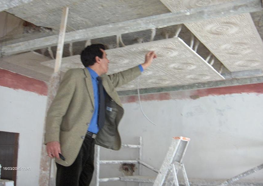 A man inspecting or working on an unfinished ceiling with exposed insulation and structural elements in a construction or renovation site.
