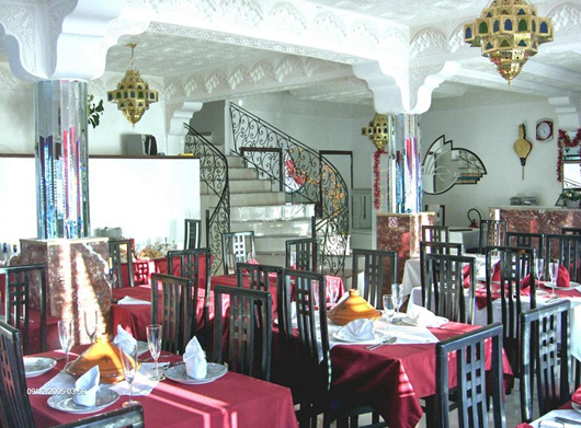 Interior of a restaurant with red tablecloths, black chairs, ornate white walls, and decorative hanging lamps.