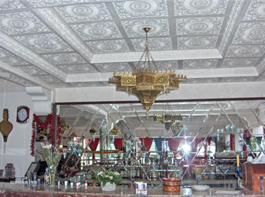 Decorative restaurant or banquet hall with ornate ceiling, chandelier, and mirrored wall, decorated for celebration with red and white floral arrangements and festive ornaments.