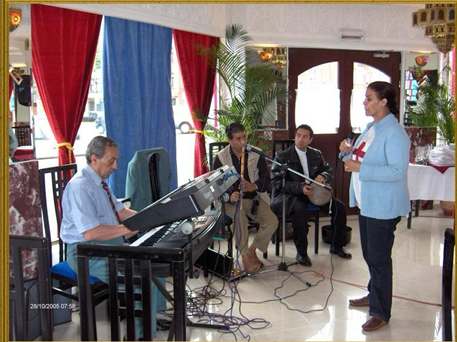 A woman in a blue blazer singing for three men sitting with musical equipment in a decorated indoor space.