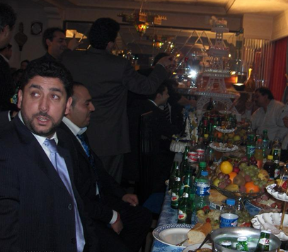 People gathered around a table with food, drinks, and fruit in a dimly lit room, possibly at a celebration or party.