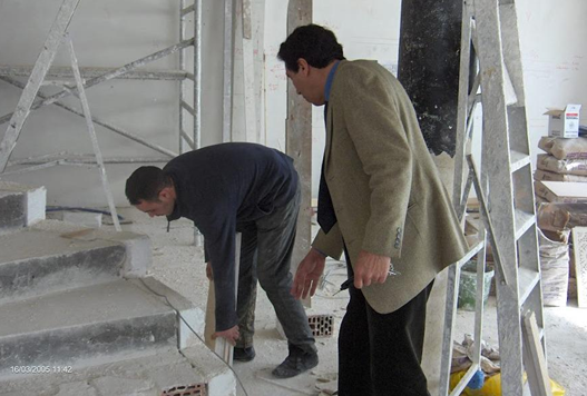 Two men inspecting or working on concrete steps at a construction site, with scaffolding and construction materials around them.