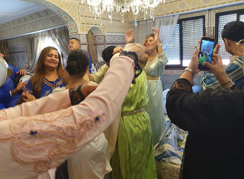 People celebrating at a party, dancing and taking photos indoors with ornate decor and chandeliers.