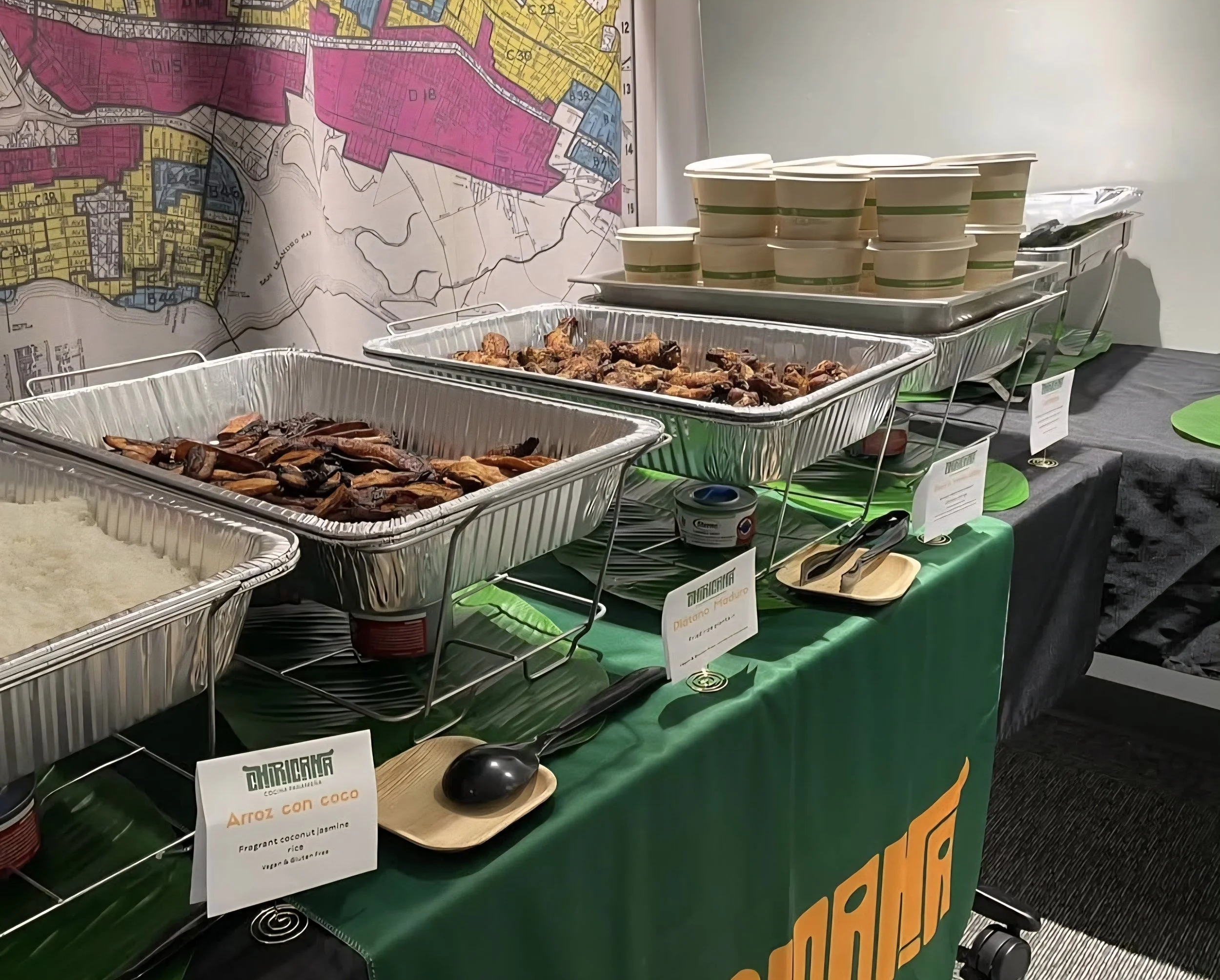 Display of food trays and cups on a table with a map in the background, indicating a food tasting or buffet setup at an event.