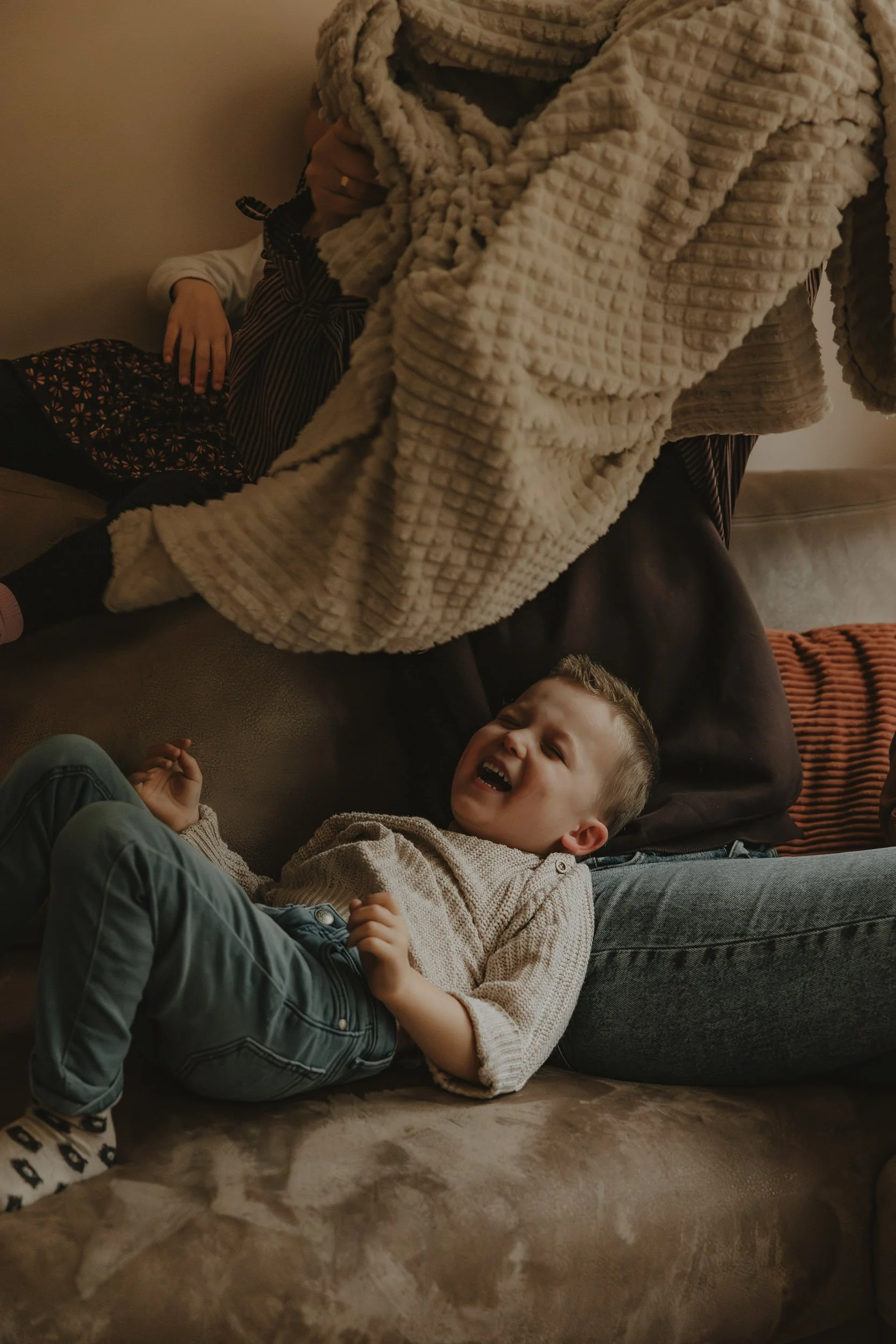 Lifestyle gezinsfotografie in Emmen – spelend kind op bank tijdens familieshoot thuis