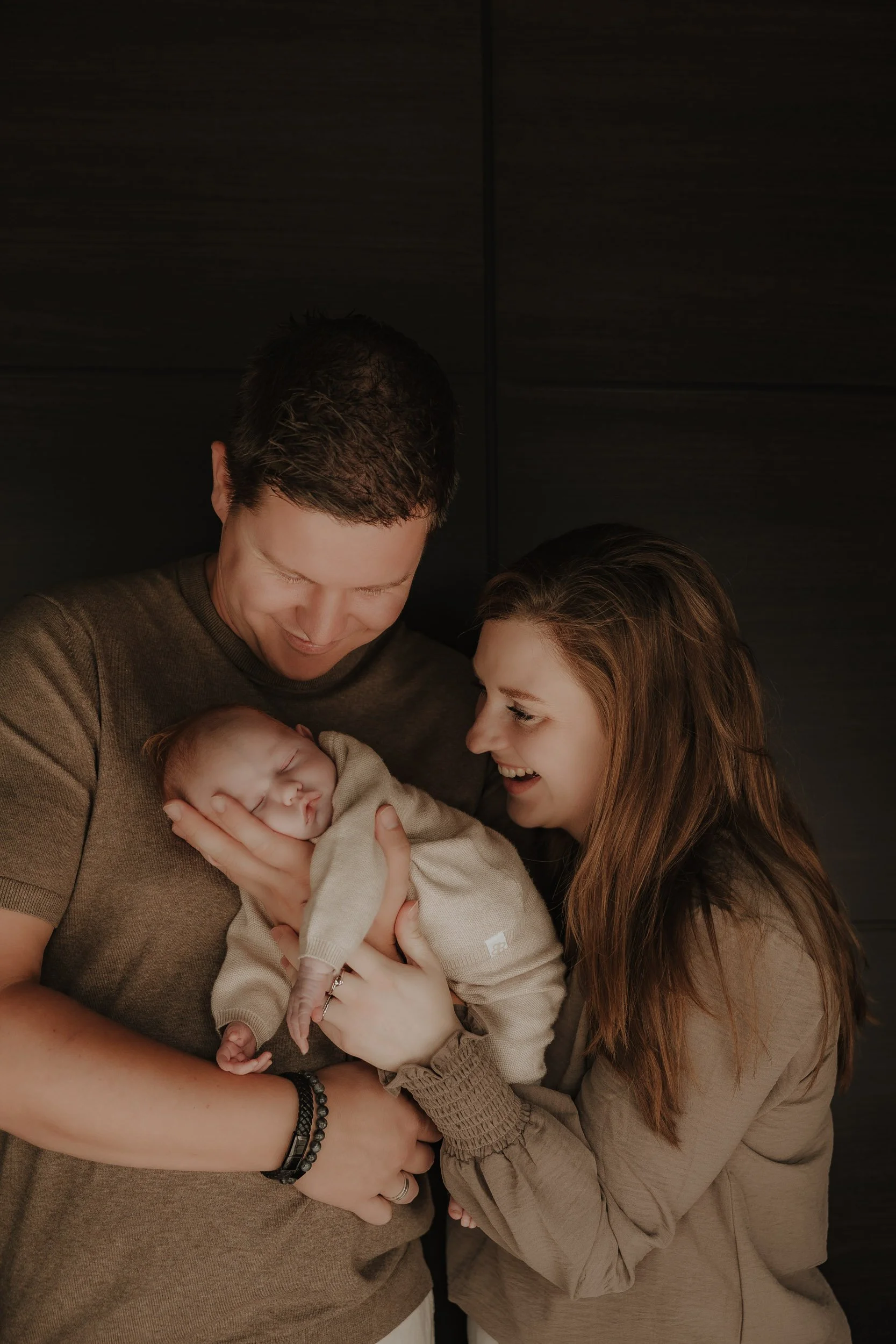Happy family with a newborn baby, parents holding and looking at the baby, smiling and sharing a joyful moment indoors.