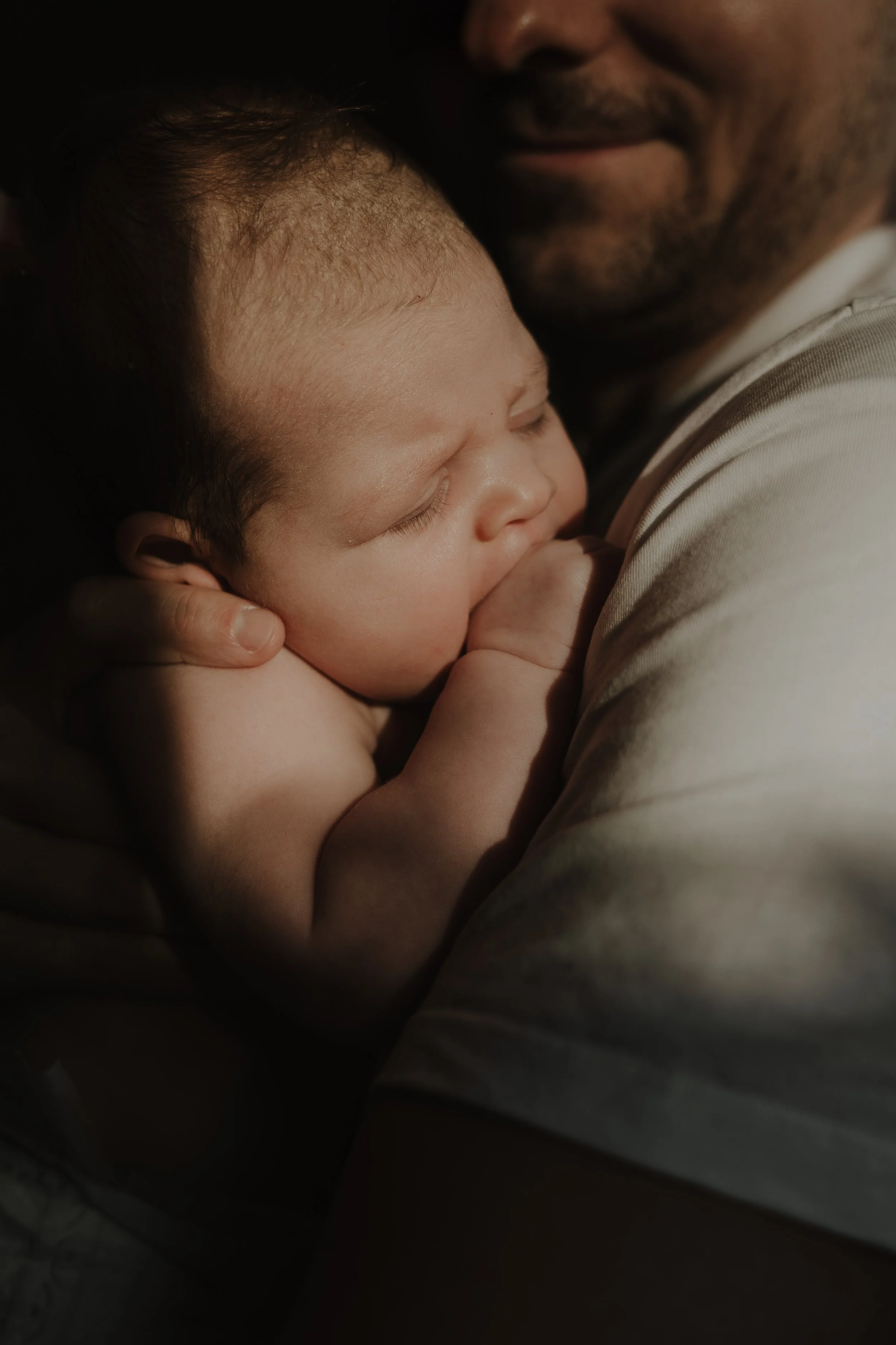 Newborn fotografie aan huis in Emmen – pasgeboren baby slaapt tegen vader aan tijdens lifestyle newborn shoot